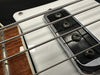 Close-up of electric bass guitar strings, pickup, and wooden fretboard with metal frets on white body guitar at Coffee House Guitars.