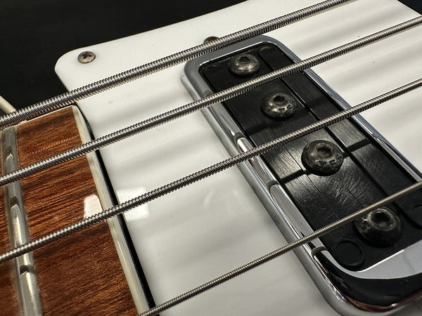 Close-up of electric bass guitar strings, pickup, and wooden fretboard with metal frets on white body guitar at Coffee House Guitars.