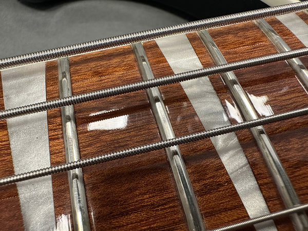 Close-up view of bass guitar fretboard with polished mother-of-pearl inlays and metal strings on glossy wood surface