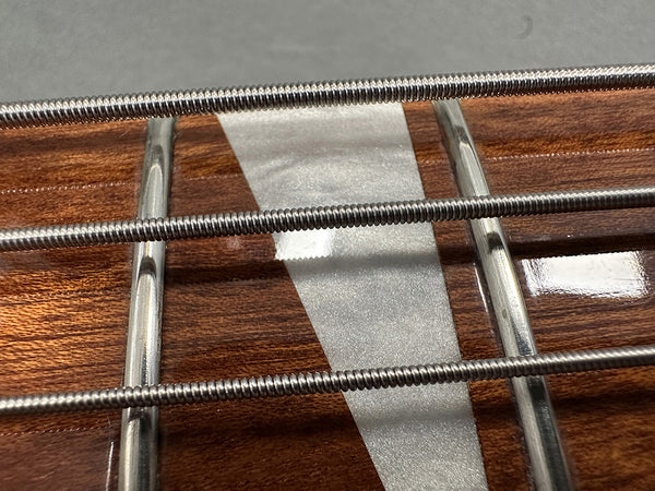 Close-up of guitar fretboard with metal frets and three wound steel guitar strings on polished wood with white inlay
