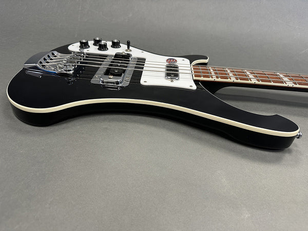 Black electric bass guitar with white pickguard and chrome hardware on gray background, angled side view