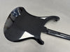 Glossy black electric guitar back and neck on gray surface showing body contour and finish reflections