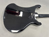 Glossy black electric guitar body with curved edges on gray surface, showing rear side and neck attachment