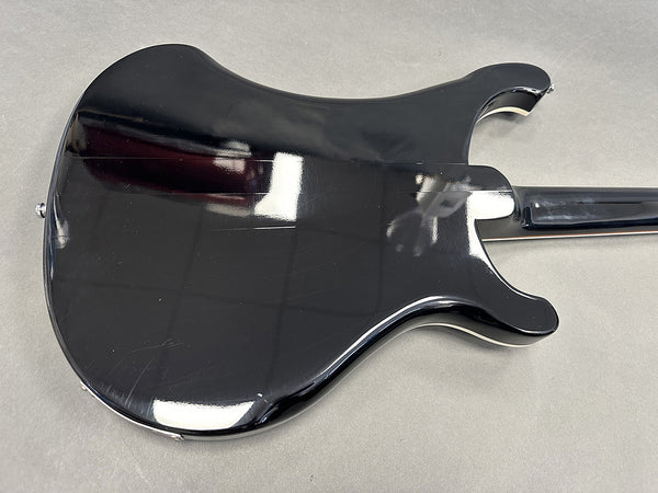 Glossy black electric guitar body with curved edges on gray surface, showing rear side and neck attachment
