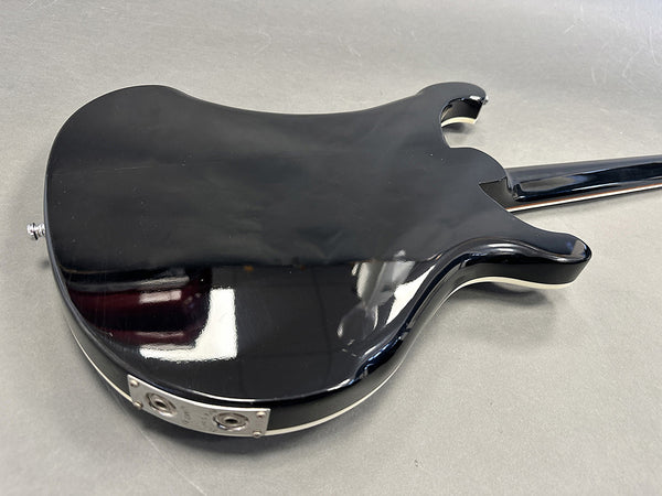 Glossy black electric guitar body with dual output jacks and white binding on a gray background