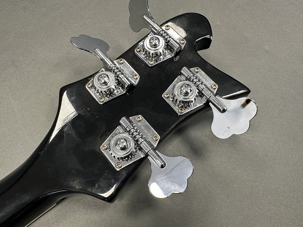 Close-up of black bass guitar headstock with four chrome tuning pegs on gray background