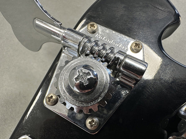 Close-up of Rickenbacker bass guitar chrome tuning machine gear and tuning key on black headstock with visible screws and engraved brand name