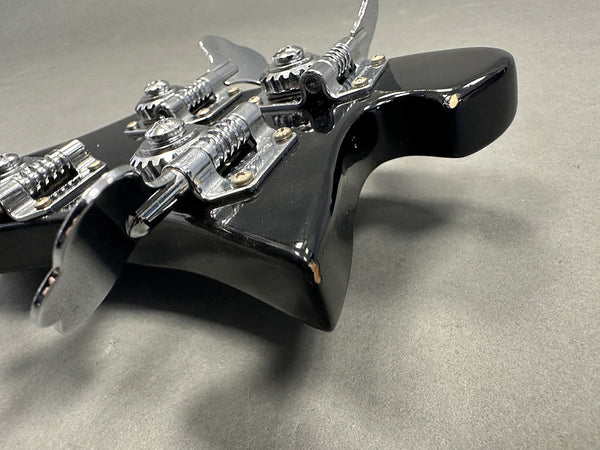 Close-up of black guitar headstock with chrome tuning pegs and visible paint chips on edges against gray background