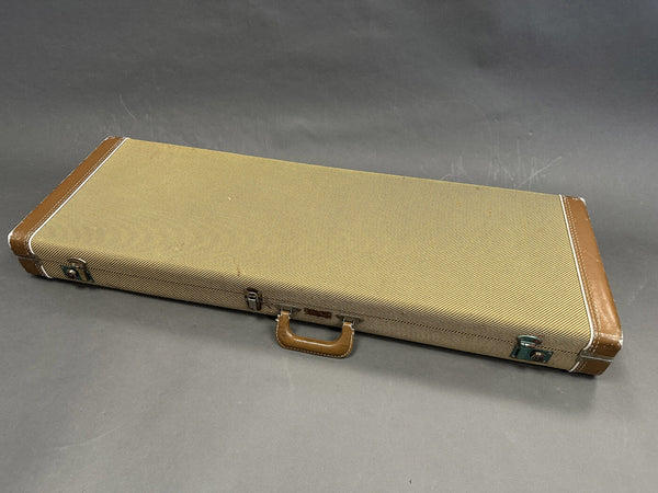 Vintage tweed guitar hard case with brown leather handle and corner reinforcements on gray background