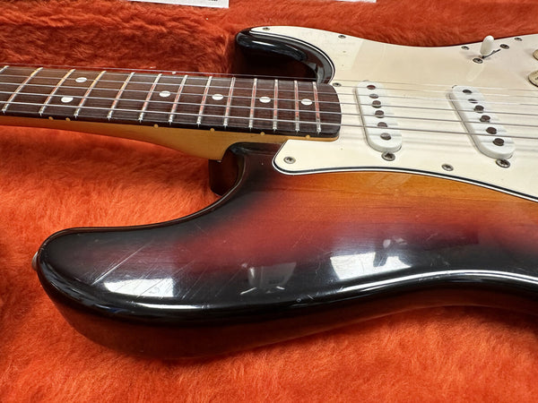 Close-up of sunburst electric guitar body and neck resting in orange plush guitar case with cream pickguard and single-coil pickups