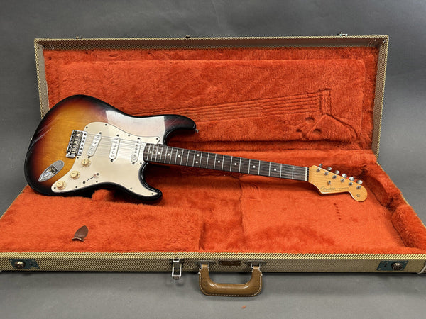 Vintage Fender Stratocaster electric guitar in sunburst finish with three single-coil pickups, maple neck, and rosewood fretboard, displayed inside a tweed hard case with orange plush interior lining.