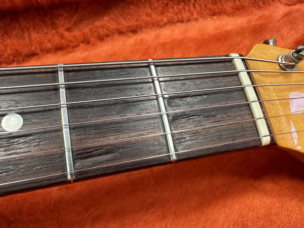 Close-up of electric guitar rosewood fretboard showing frets, strings, and dot inlay on orange fabric background