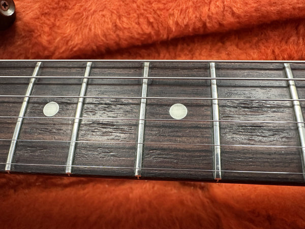 Close-up of guitar fretboard with dot inlays and six steel strings on an orange plush background