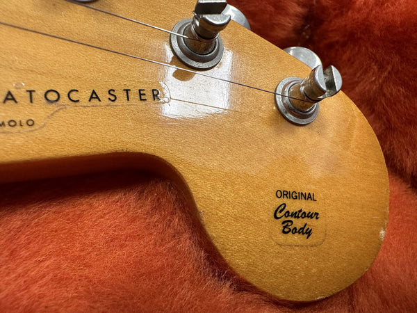 Close-up of Fender Stratocaster guitar headstock with original contour body decal and tuning pegs on orange plush background