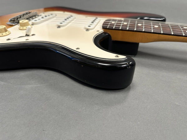 Close-up of sunburst electric guitar body and neck with white pickguard and cream control knobs on gray surface
