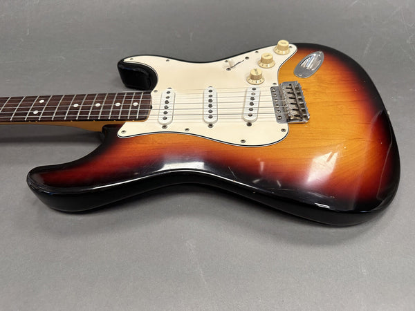 Electric guitar with sunburst finish, white pickguard, three single-coil pickups, and rosewood fretboard on gray background