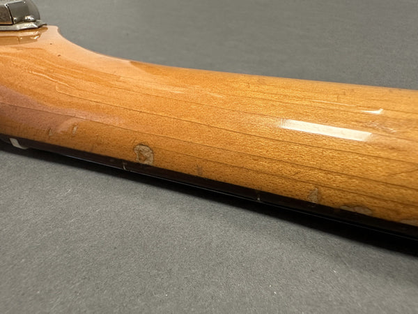 Close-up of worn and chipped maple guitar neck with visible finish wear and dents on gray background