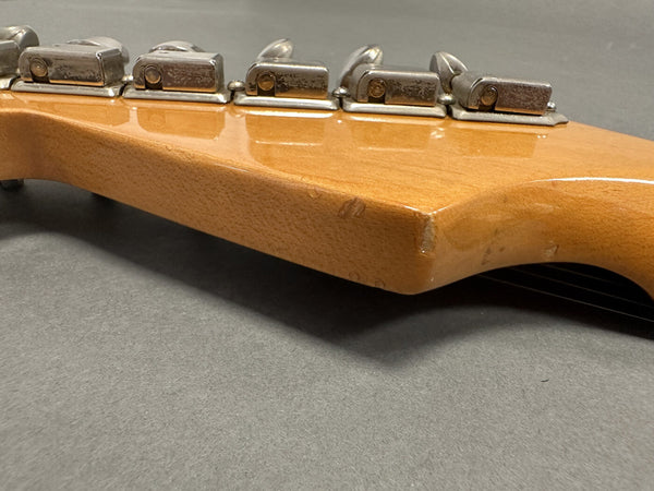 Close-up of vintage guitar headstock back showing tuning pegs and natural wood finish with minor wear and scratches on gray background