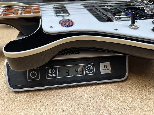 Electric guitar with American flag sticker on pickguard being weighed on digital DYMO scale showing 9 pounds 4.3 ounces