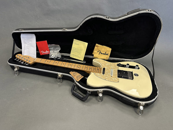 Fender electric guitar in cream with maple neck and pearl pickguard in black hardshell case with Fender polishing cloth, documentation, strings, and warranty papers displayed on gray background