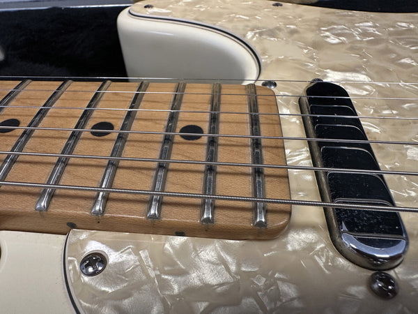 Close-up of electric guitar maple fretboard with black dot inlays, steel frets, and strings, featuring cream-colored pearloid pickguard and single-coil pickup.