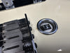 Close-up of white electric guitar bridge and input jack with metal string ends and adjustment springs visible for precise tuning.