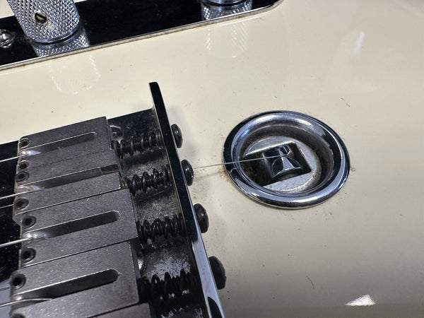 Close-up of white electric guitar bridge and input jack with metal string ends and adjustment springs visible for precise tuning.