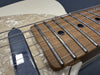 Close-up of electric guitar fretboard, metal frets, black dot inlays, pearl pickguard, and single-coil pickup with six steel strings on a cream-colored body