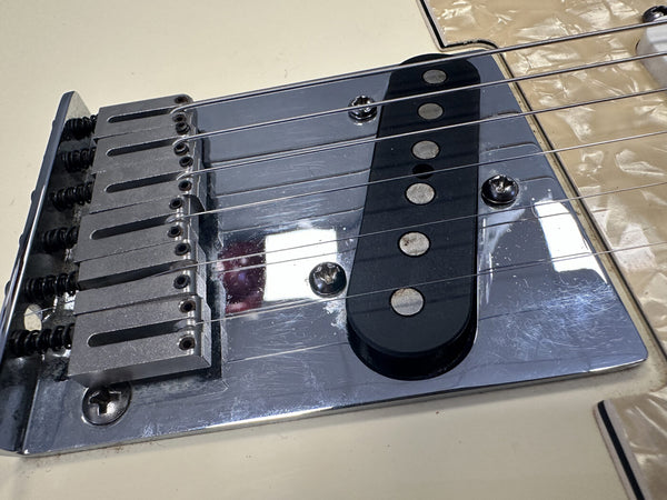 Close-up of vintage electric guitar bridge and single-coil pickup with six strings and metal saddle pieces on cream body