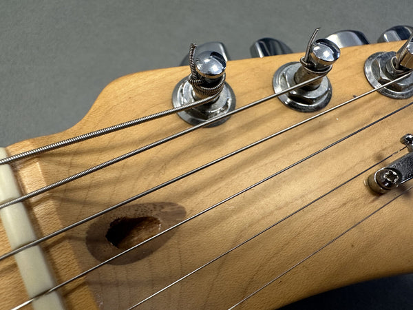 Close-up of natural wood guitar headstock with chrome tuning pegs and metal strings wrapped around tuning posts on gray background