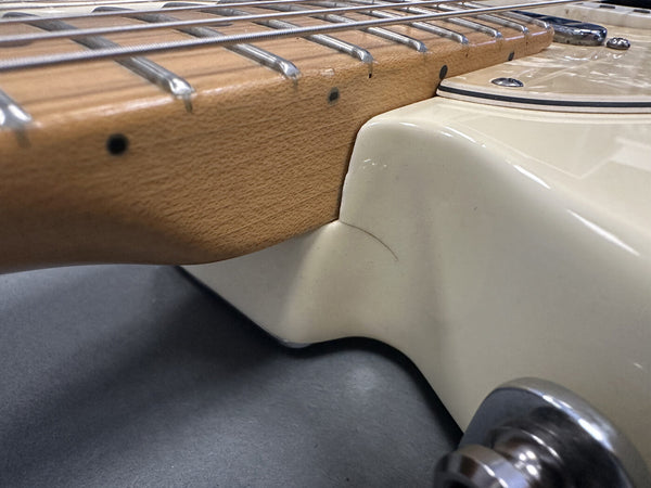 Close-up of guitar neck joint and frets with cream-colored body and visible surface crack near neck heel, showcasing detailed wood grain and metal hardware.