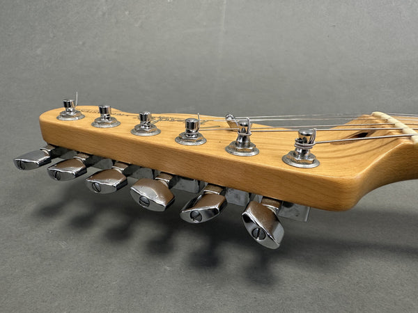 Close-up of electric guitar maple headstock with chrome tuning pegs and strings against gray background