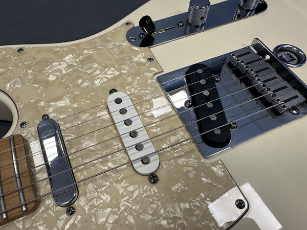 Close-up of electric guitar strings, pickups, and metallic bridge on cream-colored body with pearloid pickguard at Coffee House Guitars.