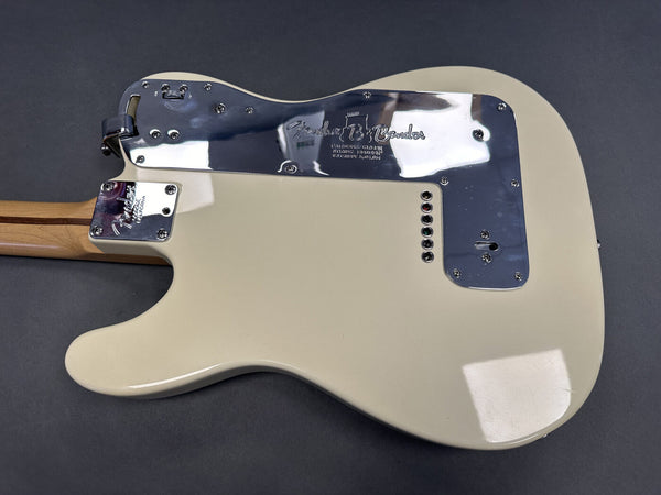 Fender electric guitar back view showing cream-colored body, chrome guitar neck plate, and chrome backplate with Fender logo and string ferrules on dark gray background.
