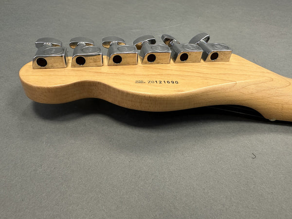 Close-up of maple guitar headstock back showing six chrome tuning pegs and serial number Z0121690 on gray background