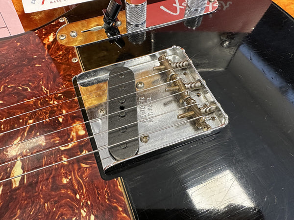 Close-up of Fender electric guitar vintage style bridge with six metal saddles and black single-coil pickup on black and tortoiseshell pickguard body