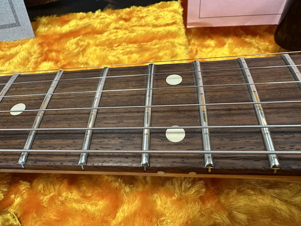 Close-up of guitar fretboard with metal frets and dot inlays on a wooden neck over orange fuzzy background