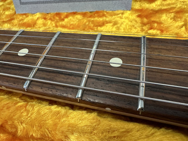 Close-up of guitar fretboard with metal frets and dot inlays, resting on a yellow plush case lining