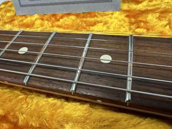 Close-up of guitar fretboard with metal frets and white dot inlays on a wooden neck, resting on a vibrant yellow plush surface.