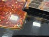 Close-up of vintage electric guitar pickguard with tortoiseshell pattern and nearby pickup on glossy black body showing scratches and wear