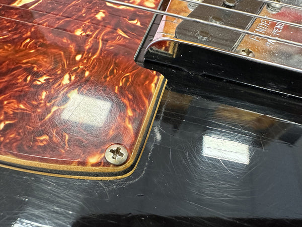 Close-up of vintage electric guitar pickguard with tortoiseshell pattern and nearby pickup on glossy black body showing scratches and wear