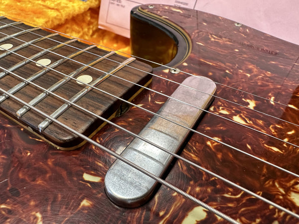 Close-up of vintage electric guitar with tortoiseshell pickguard, metal pickup cover, and rosewood fretboard with dot inlays and steel strings