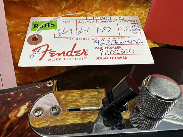 Fender guitar control knobs with a Fender inspection tag showing part number B102300 and serial number 9237000432 on a gold plush guitar case interior