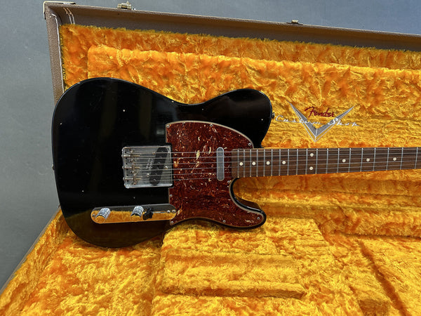 Black Fender Custom Shop Telecaster electric guitar with tortoiseshell pickguard resting in yellow plush-lined Fender vintage hard case