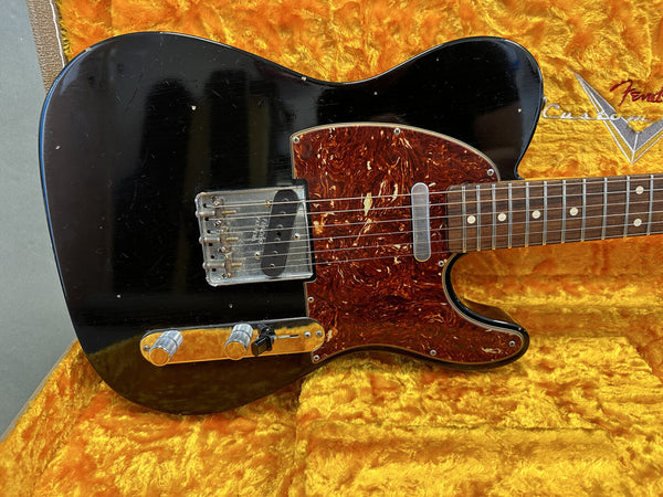 Close-up of black Fender Telecaster electric guitar body with tortoiseshell pickguard and chrome hardware in a yellow plush case interior