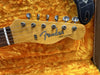 Close-up of Fender Telecaster guitar headstock with tuning pegs, resting on bright orange plush guitar case lining with visible guitar strap end