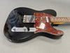 Black electric guitar with tortoiseshell pickguard, chrome hardware, and maple neck on gray background