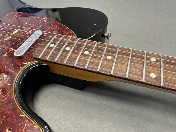 Close-up of electric guitar neck and fretboard with dot inlays, black body, and tortoiseshell pickguard.