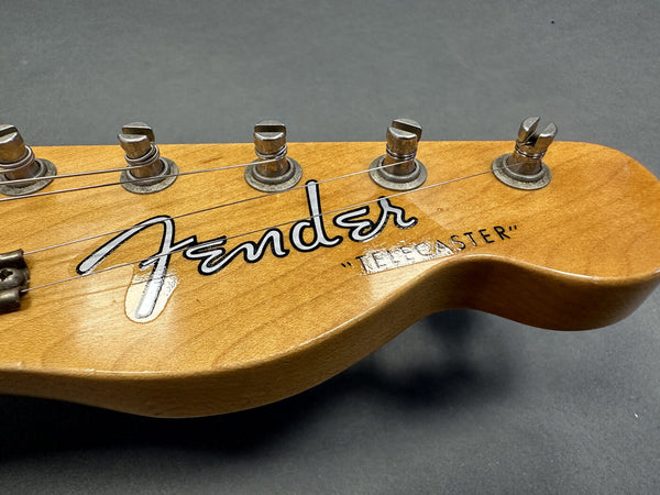 Close-up of natural wood Fender Telecaster guitar headstock with six tuning pegs and strings on gray background