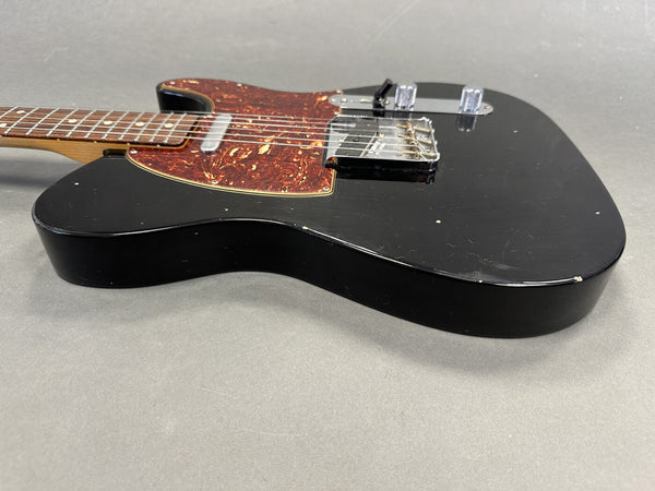 Black electric guitar with tortoiseshell pickguard and chrome hardware on gray background, showing body and lower neck